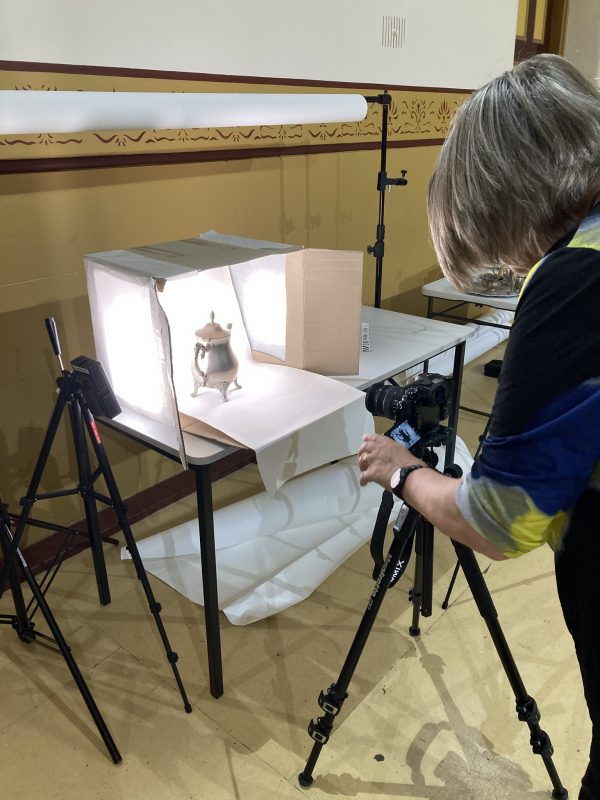 Close up of a person photographing a silver jug in a light box