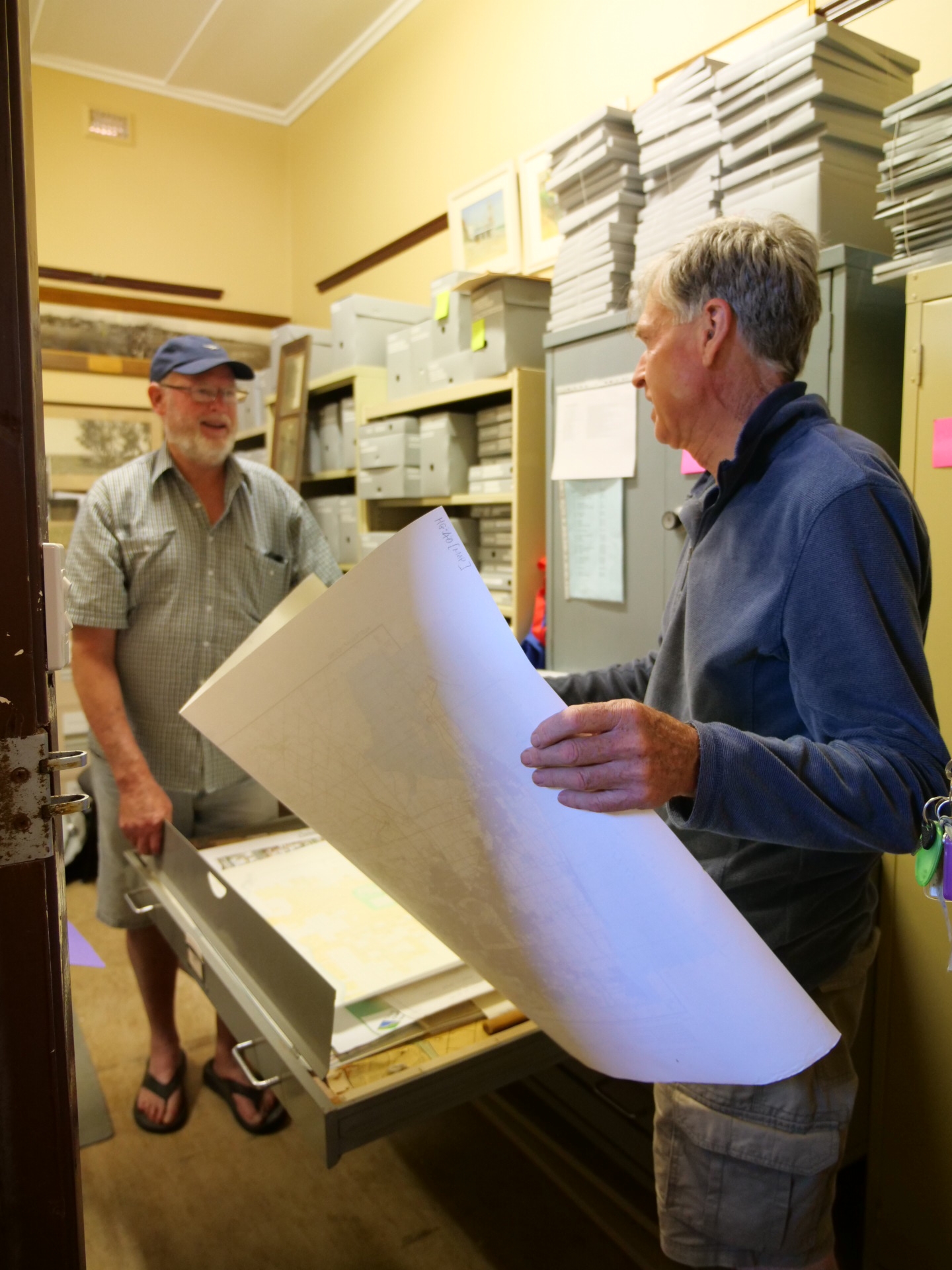 Two men in a storage space with shelves full of archive